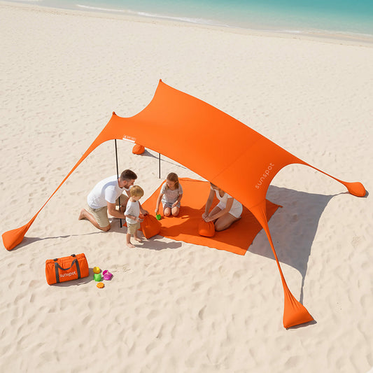 Orange tent on a sandy beach with people and toys around